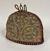 An Eastern burgundy padded wool crescent shaped tea cosy with gilt braided top with three loops