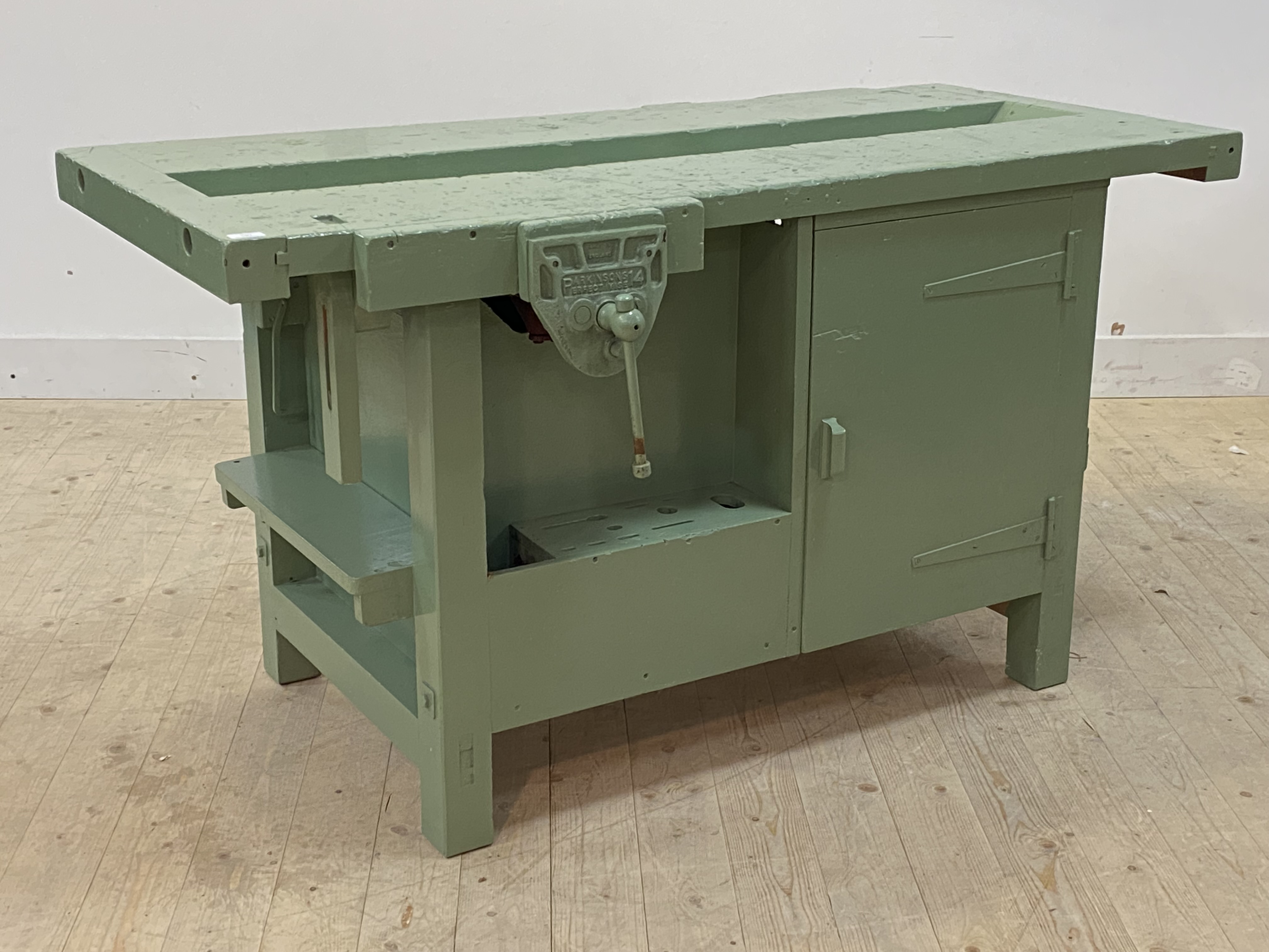 A green painted hardwood and plywood work bench, the channelled top over vice, two cupboards and