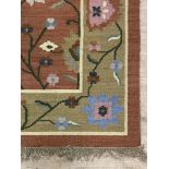 An Indian wool and cotton flat weave rug, the burnt orange field with stylised trailing foliate