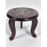 A stained mahogany circular topped three leg stool with relief carved radiating leaf decoration to