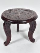 A stained mahogany circular topped three leg stool with relief carved radiating leaf decoration to