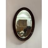 An early 20th century mahogany framed oval wall mirror, the frame with 'C' scrolled moulding