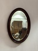 An early 20th century mahogany framed oval wall mirror, the frame with 'C' scrolled moulding