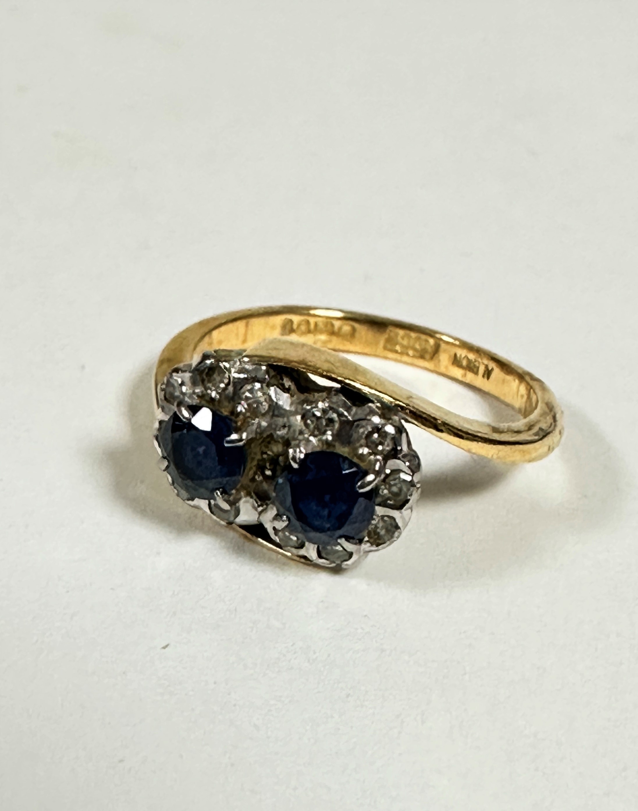 An 18ct gold two stone sapphire cross over ring, each circular cut sapphire is approximately .