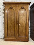 A Victorian mahogany wardrobe, the projecting cornice over two arched doors enclosing a silk lined