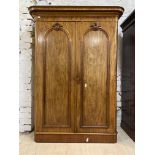 A Victorian mahogany wardrobe, the projecting cornice over two arched doors enclosing a silk lined