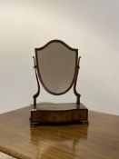 An Edwardian walnut vanity mirror, the mirror of shield form swivelling between two scrolled