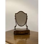 An Edwardian walnut vanity mirror, the mirror of shield form swivelling between two scrolled