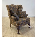 A large wingback chair of 18th century design, upholstered in floral fabric, raised on leaf carved