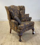 A large wingback chair of 18th century design, upholstered in floral fabric, raised on leaf carved