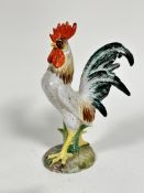 A pottery cockerel decorated with polychrome enamels, raised on shaped moulded base, (h 33cm x