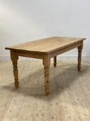 A large pine farmhouse dining table, the scrub top over plain frieze raised on turned supports,