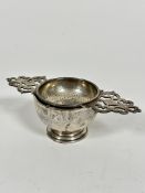A London 1953 silver tea strainer with pierced C scroll design, complete with circular stand, on