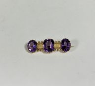 A late Victorian three-stone amethyst bar brooch, the central cushion-cut amethyst claw-set