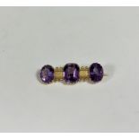 A late Victorian three-stone amethyst bar brooch, the central cushion-cut amethyst claw-set