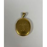 A late 19th century gold (unmarked) locket, oval, opening to twin glazed compartments, engraved to