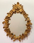 A carved giltwood oval wall mirror, the frame formed as repeating flower heads and trailing oak