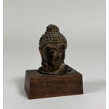 A South-East Asian bronze head of a Buddha (a fragment of a larger figure), mounted on a wooden