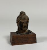 A South-East Asian bronze head of a Buddha (a fragment of a larger figure), mounted on a wooden