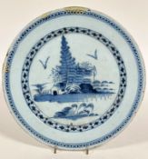 An 18thc Dutch Delft plate, the centre circular panel with stylised pine trees and building enclosed