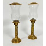 A pair of brass turned column storm lanterns with shaped glass shades, complete with domed cover, (