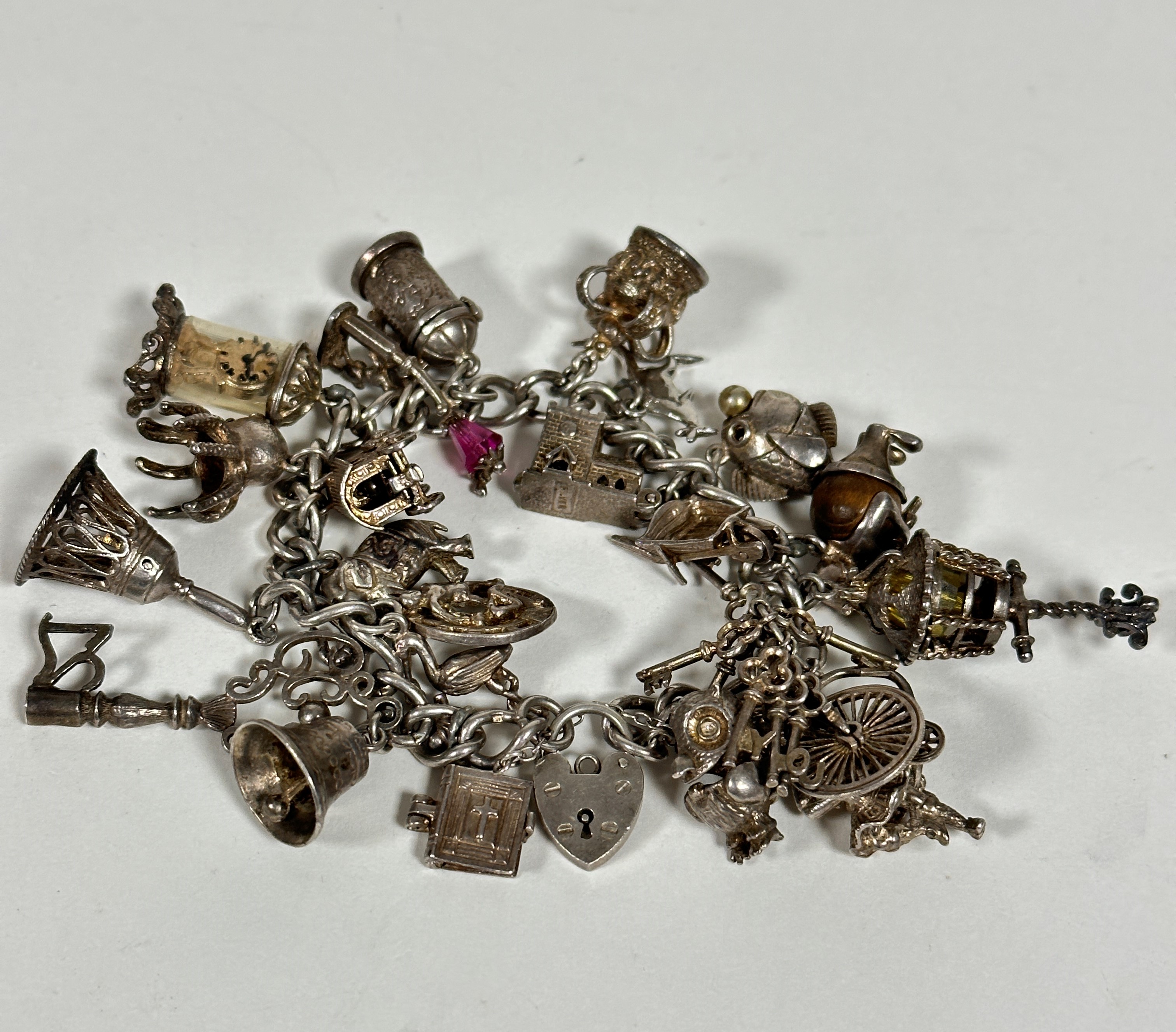 A silver curb link bracelet mounted with a large collection of silver charms including a key, bells,