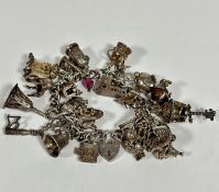 A silver curb link bracelet mounted with a large collection of silver charms including a key, bells,