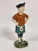 A late 19thc early 20thc pottery figure of a young boy in Scottish traditional dress with blue tammy
