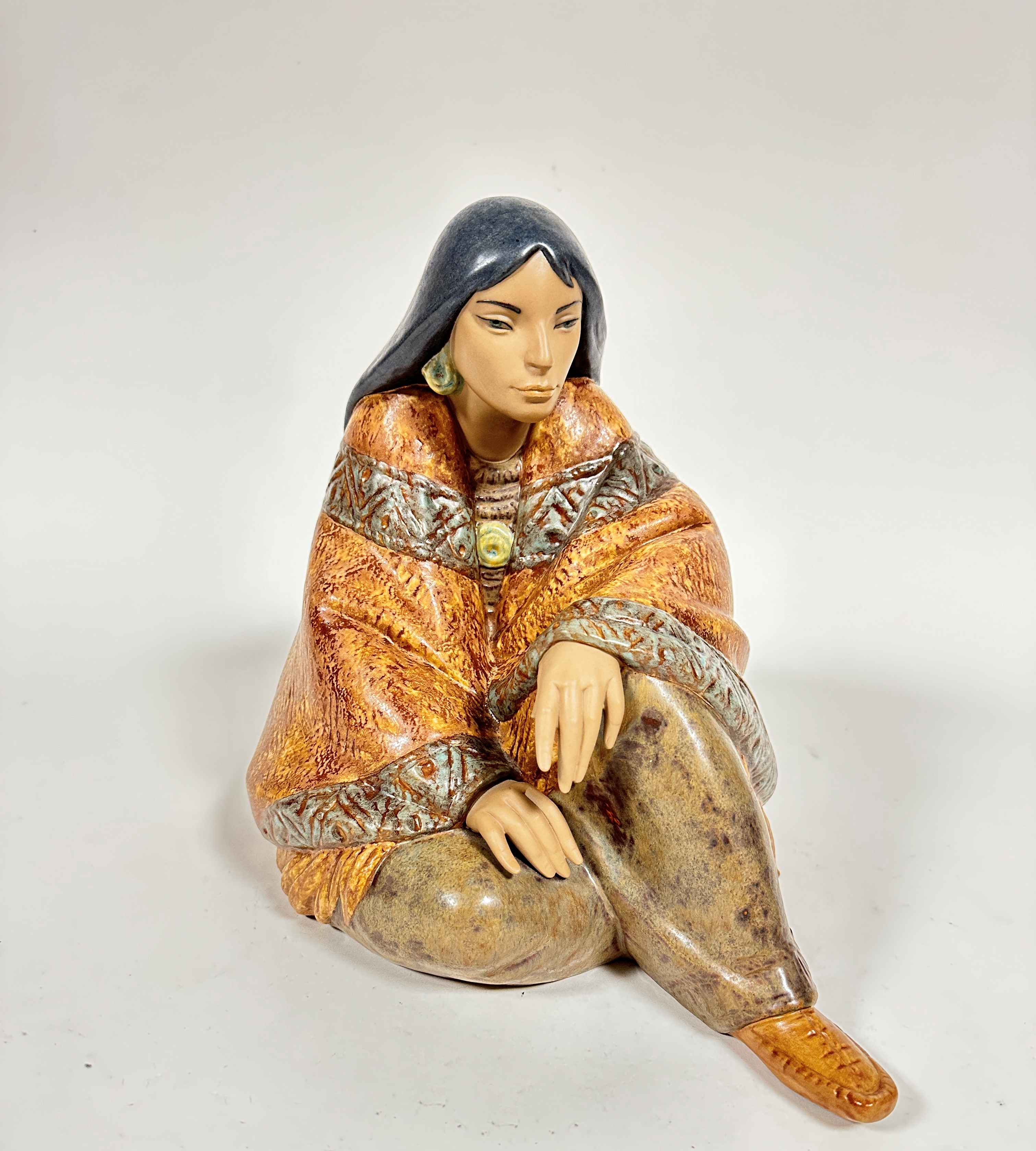 A Spanish Lladro pottery figure of a seated Mexican lady draped with shawl and moccasins,