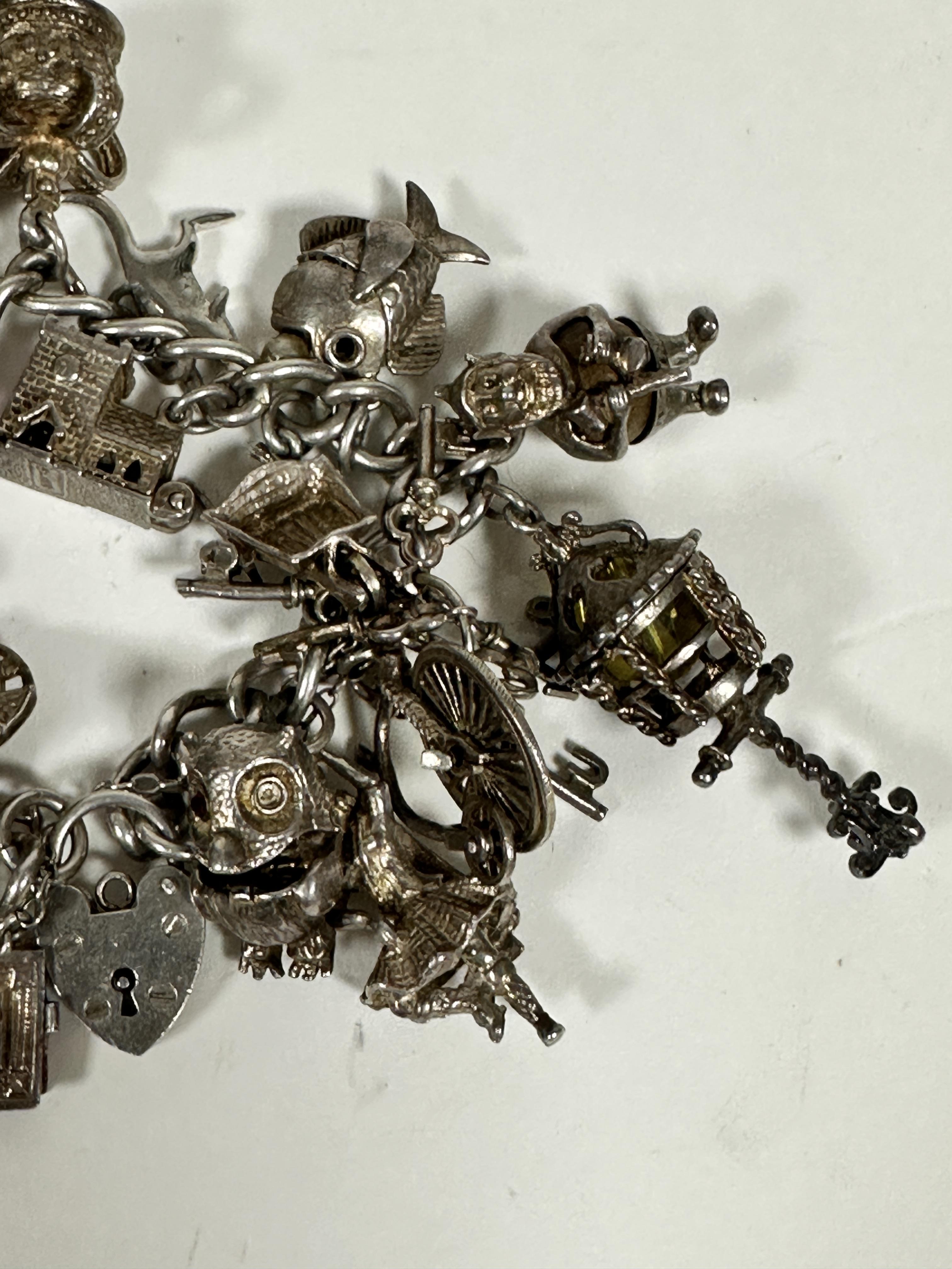 A silver curb link bracelet mounted with a large collection of silver charms including a key, bells, - Image 2 of 4