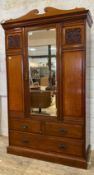 An Edwardian mahogany wardrobe, the swan neck pediment over bevel glazed mirror door opening to an