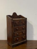 A stained pine table top miniture chest, fitted with two short and three long graduated drawers,