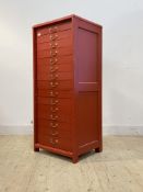 A red painted collectors chest, fitted with 15 drawers and panelled sides, raised on stile supports.