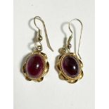 A pair of Victorian style oval garnet cabouchon earrings mounted in scrolling rope pattern border,