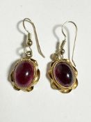 A pair of Victorian style oval garnet cabouchon earrings mounted in scrolling rope pattern border,