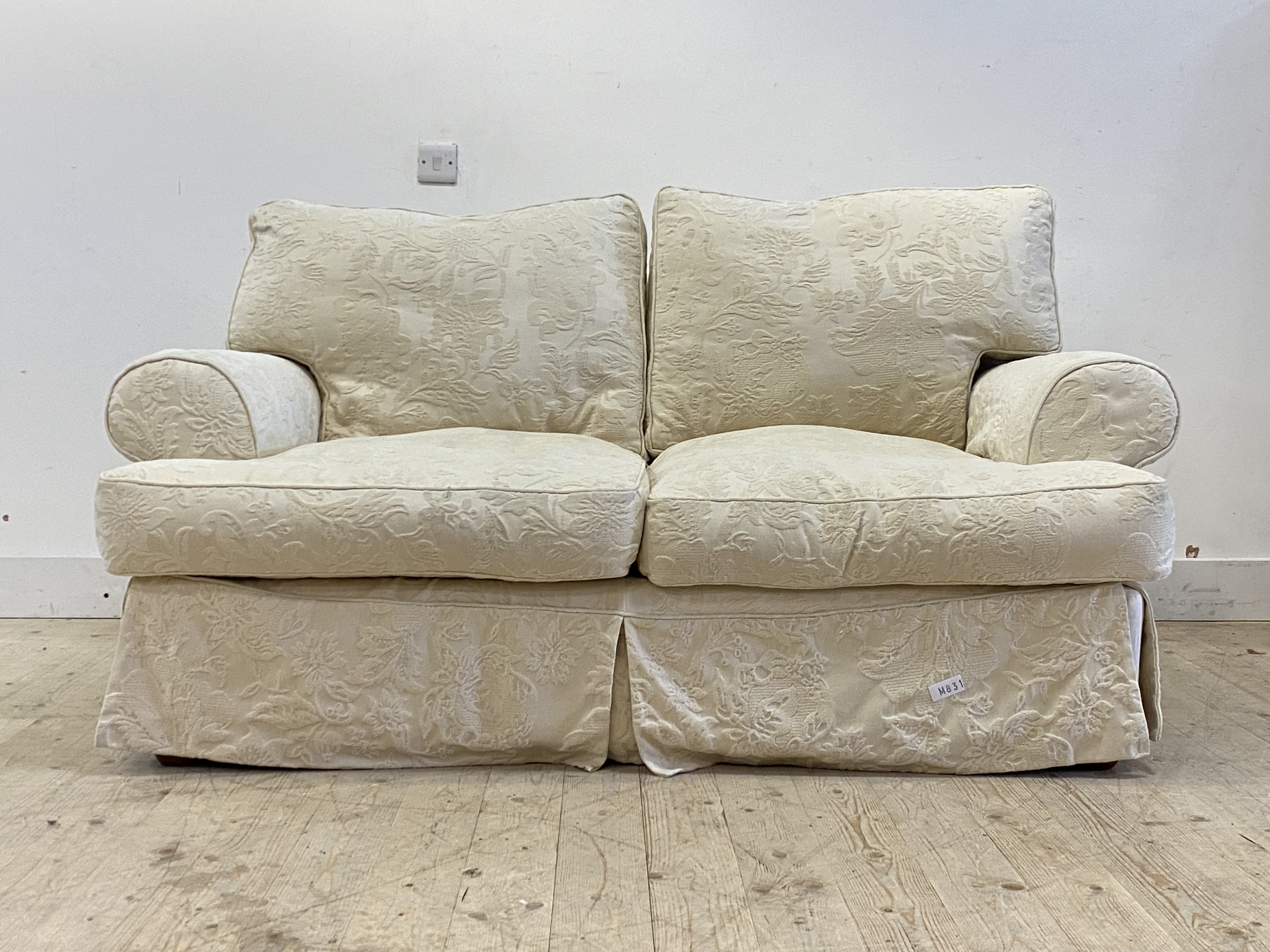 A traditional two seat sofa, upholstered in a fitted white demask cover, raised on turned bun