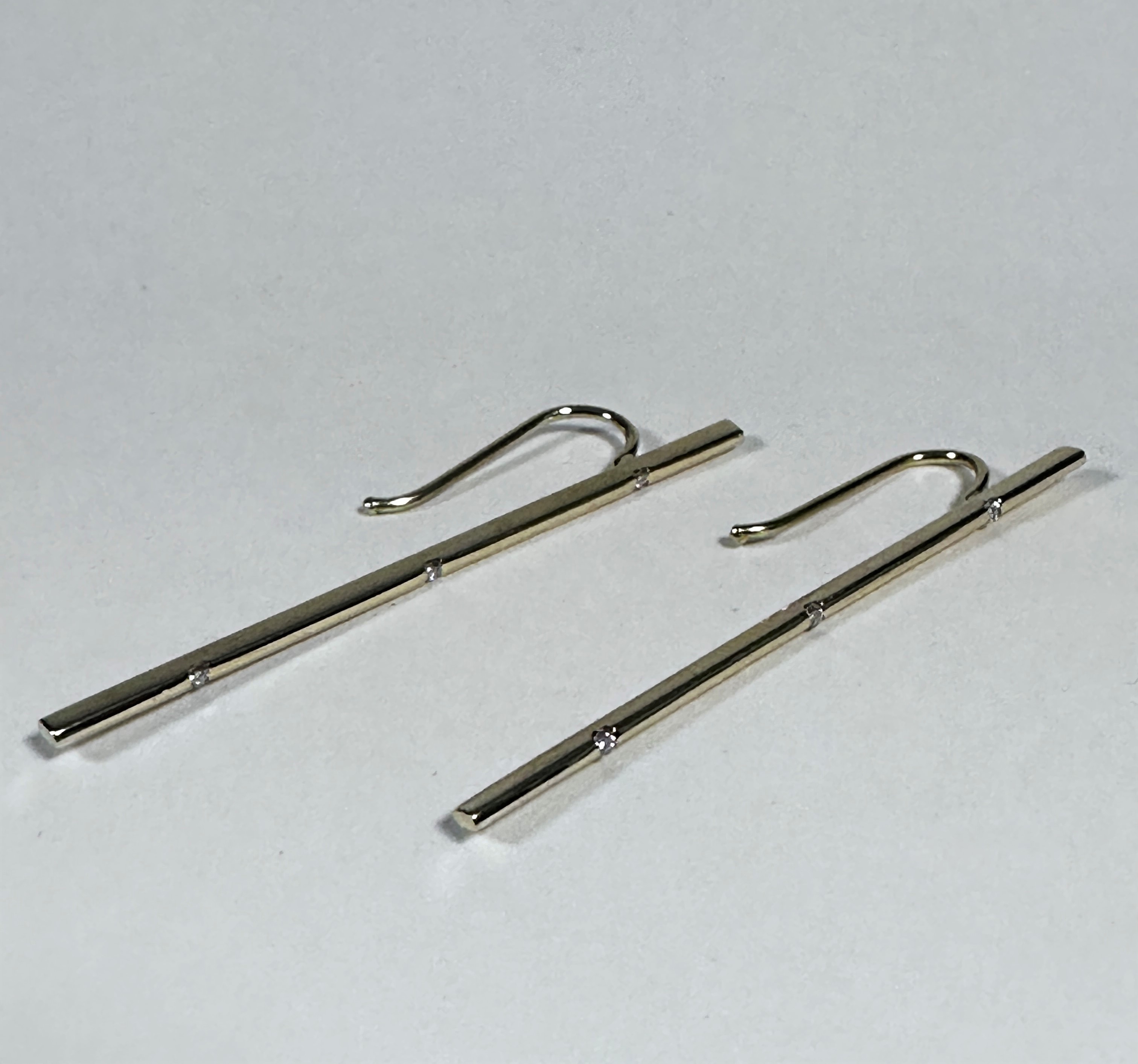 A pair of knife edge pendant drop earrings set three diamond points, with arched fittings, (L: 5cm x