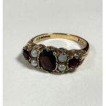 A 9ct gold three stone garnet ring set four half seed pearls, mounted in claw setting with chased