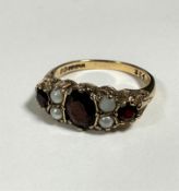 A 9ct gold three stone garnet ring set four half seed pearls, mounted in claw setting with chased