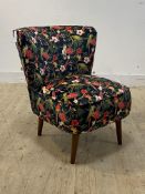 A contemporary bedroom chair, upholstered in overstuffed velvet printed with tropical birds,