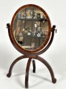 A 19thc mahogany oval dressing mirror on folding bipod support, with scroll suppots, (41cm x 28cm)