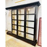 A large contemporary ebonised ash glazed cabinet, the dentil cornice over three doors, each