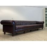 An impressive Chesterfield bench sofa, upholstered in deep buttoned brown leather, raised on