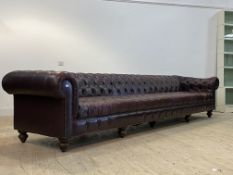 An impressive Chesterfield bench sofa, upholstered in deep buttoned brown leather, raised on