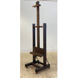 A 19th century French oak easel, the frame rising on a screw handle, moving on castors, with Paris