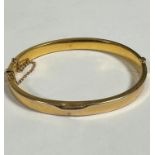 A hollow 9ct gold oval engraved stiff hinged bangle complete with safety chain, (0.5cm x 7cm x 5.