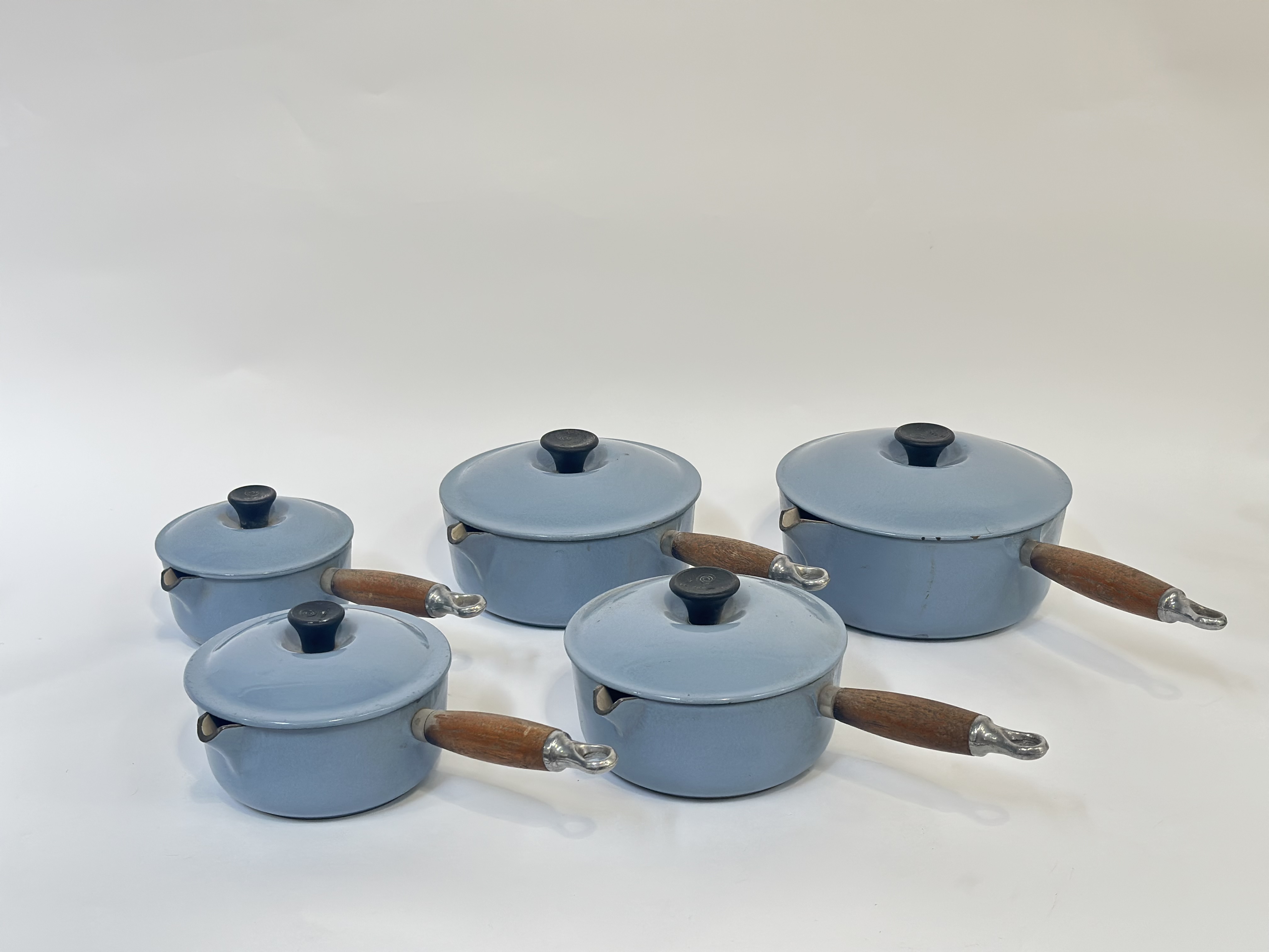 A group of five Le Creuset cast iron pans with duck egg blue enamelling with wooden handles,