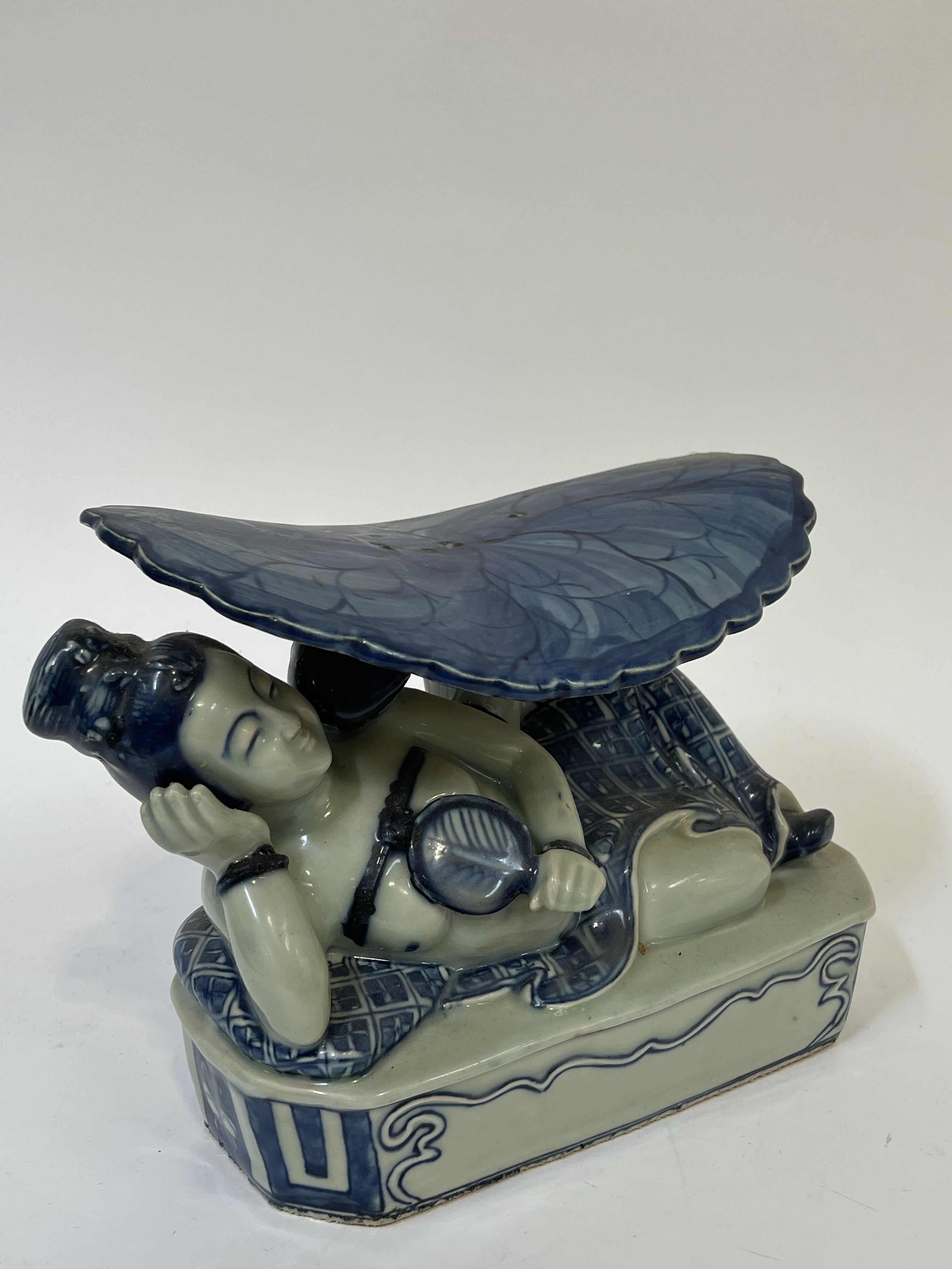 A modern Chinese blue and white porcelain headrest/pillow modeled as a reclining female under a
