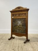 An Edwardian floral carved walnut fire screen, having a glazed oil on canvas panel depicting a