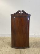 A Georgian mahogany bow front wall hanging corner cabinet, with swan neck pediment over dentil